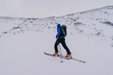 Fototapeta na wymiar Ski alpinist ascending a snow slope in the alps. Winter alpine mountain landscape and ski touring adventure activity. Ski alpinism in the Alpine mountain area, Europe.