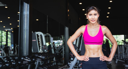 Fototapeta na wymiar Portrait of young pretty Asian girl with six packs in sportswear standing and crossing arms at fitness gym with copy space. fitness work out and yoga health concept