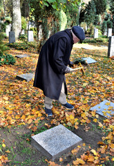Rentner harkt Laub auf dem Friedhof