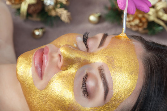 Beautician makes a golden mask to rejuvenate the skin to beautiful woman. Next to her are Christmas decorations.New Year's and Cosmetology concept.