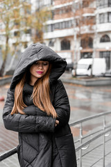beautiful girl with makeup in a black jacket in a hood under the rain