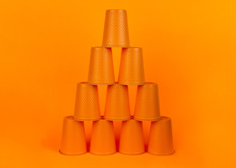 Pyramid of orange plastic disposable cups on an orange background. Waste concept. Minimal space.