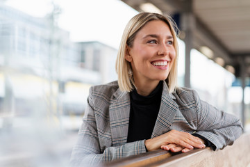 Happy young businesswoman at the train station looking around