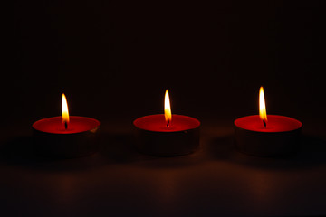 Three small pink wax decorative candles burn on a dark background.