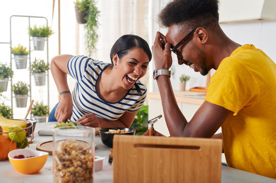 Multiethnic couple laughing, breakfasting together in the kitchen