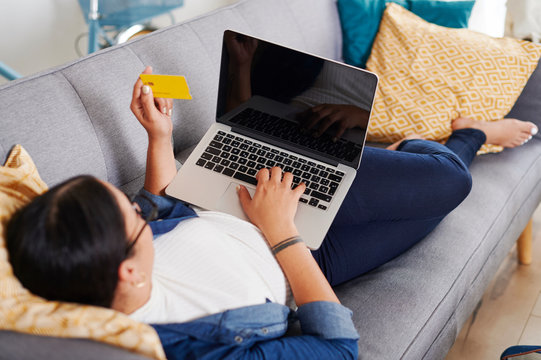 Young woman using laptop and lying on a sofa