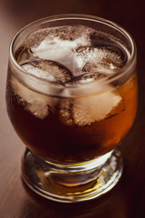 Glass of whiskey with ice on dark wood background. Alcohol beverage. Single object. Macro shot.