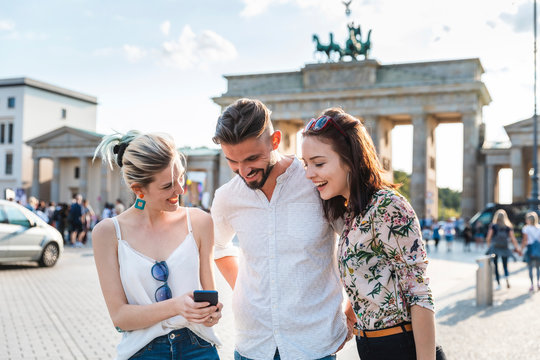 Three friends looking at cell phone in front of Brandenburger Tor, Berlin, Germany