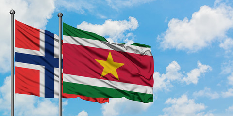 Bouvet Islands and Suriname flag waving in the wind against white cloudy blue sky together. Diplomacy concept, international relations.