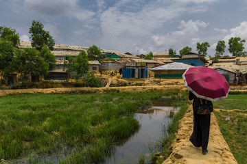 joven rohingya paseando con sombrilla tras el monzon en campo refugiados. problemas migrantes migracion crisis
