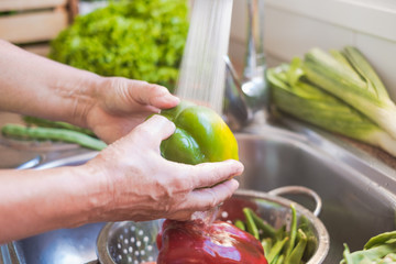 The water flows over a sink full of vegetables to wash. Close up view of a green pepper. One people only