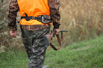 Hunting period, autumn season open. A hunter with a gun in his hands in hunting clothes in the autumn forest in search of a trophy. A man stands with weapons and hunting dogs tracking down the game.	