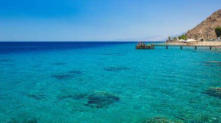Fototapeta premium summer vacation luxury destination of Red sea bay Aqaba Gulf near Israeli city Eilat picturesque tropic shore line with coral reefs on bottom and pier on background, copy space 