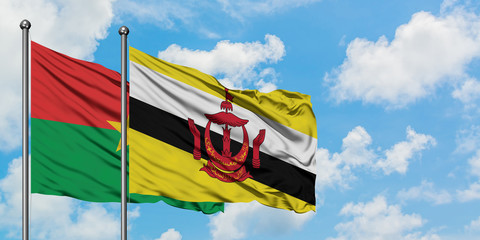 Burkina Faso and Brunei flag waving in the wind against white cloudy blue sky together. Diplomacy concept, international relations.