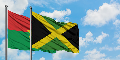 Burkina Faso and Jamaica flag waving in the wind against white cloudy blue sky together. Diplomacy concept, international relations.