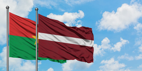 Burkina Faso and Latvia flag waving in the wind against white cloudy blue sky together. Diplomacy concept, international relations.