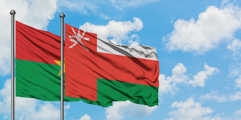 Burkina Faso and Oman flag waving in the wind against white cloudy blue sky together. Diplomacy concept, international relations.
