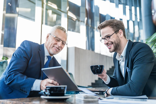Senior businessman using digital tablet and discuss information with young man in suit on a meeting