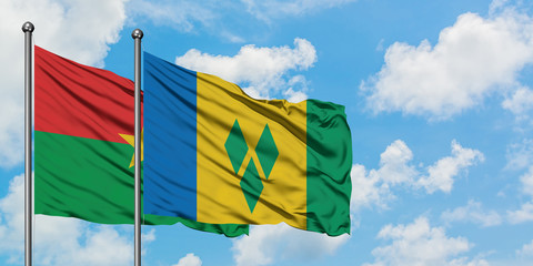 Burkina Faso and Saint Vincent And The Grenadines flag waving in the wind against white cloudy blue...