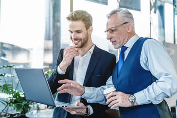 Two cheerful business professional looking at laptop computer at coffee shop