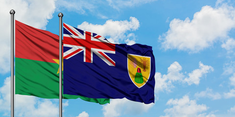 Burkina Faso and Turks And Caicos Islands flag waving in the wind against white cloudy blue sky together. Diplomacy concept, international relations.