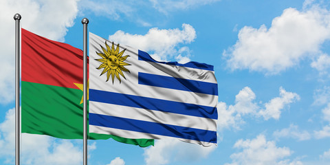 Burkina Faso and Uruguay flag waving in the wind against white cloudy blue sky together. Diplomacy concept, international relations.