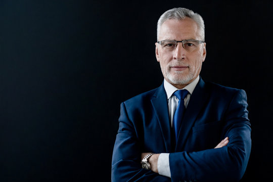 Portrait of mature businessman in suit and eyeglasses on black background