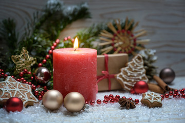 Christmas arrangement with a red burning candle, fir branches, baubles and ornaments in the snow against a wooden background