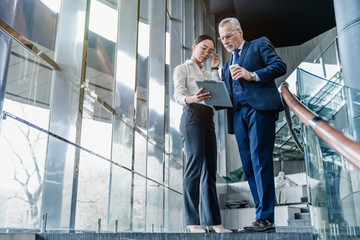 Two business partners holding documents and discussing business plans together while standing at...