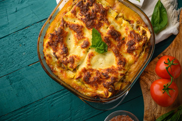 Ready Italian lasagna, on a green wooden background with basil, tomatoes. Culinary background, Italian recipe book, delicious food. With space for design, top view.