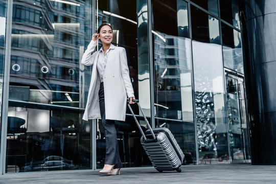 Full length portrait of traveling young woman with suitcase outside