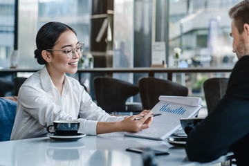 Asian businesswoman holding a paper in hand and showing analitics while talking to her business...