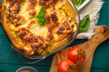 Ready Italian lasagna, on a green wooden background with basil, tomatoes. Culinary background, Italian recipe book, delicious food.
