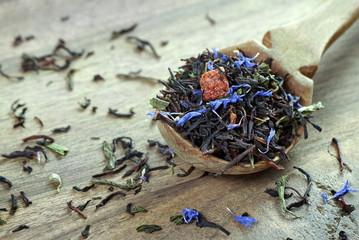 blended tea. black tea with dry flower petals and fruits. dry black tea leaves in a wooden spoon....