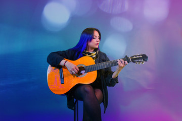 Naklejka na ściany i meble Latin woman playing an acoustic guitar on purple background with drained blue and light sparkles