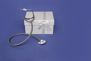 medical device for listening to a stethoscope and a beautiful box with a bow, gift, on a blue background, concept of physician's day, close-up, copy space