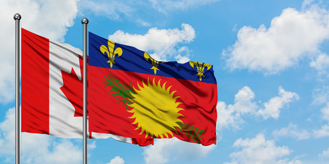 Canada and Guadeloupe flag waving in the wind against white cloudy blue sky together. Diplomacy...