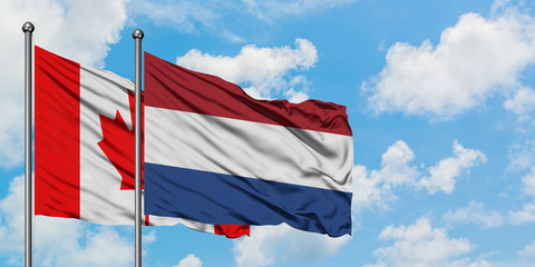Canada and Netherlands flag waving in the wind against white cloudy blue sky together. Diplomacy concept, international relations.