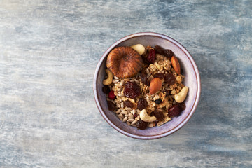 Bowl of granola with nuts, raisins and fig. Concept for a tasty and healthy meal. Rustic wooden background. Top view. Copy space. 