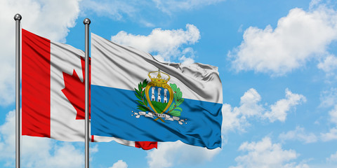 Canada and San Marino flag waving in the wind against white cloudy blue sky together. Diplomacy concept, international relations.