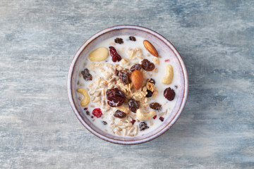 Bowl of granola with milk, nuts, raisins and cranberries. Concept for a tasty and healthy meal. Rustic wooden background. Top view. Close up. Copy space. 