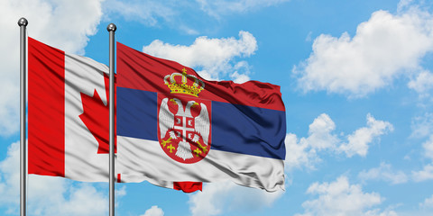 Canada and Serbia flag waving in the wind against white cloudy blue sky together. Diplomacy concept, international relations.