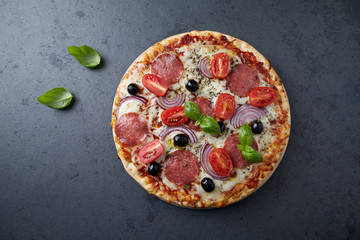 Pizza with salami, mozzarella cheese, cherry tomatoes, black olives, red onion and oregano. Home made food. Concept for a tasty and hearty meal. Black stone background. Top view. Copy space