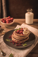 Pancakes with raspberries, banana slices, pomegranate seeds and honey