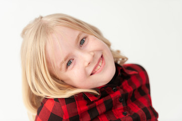 Close up of a smiling young blonde preteen girl with head tilted on a white studio background