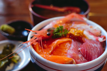 Soft,selective focus of Japanese food rice bowl with sashimi, fish, Salmon, and shrimp, seafood rice bowl on top of sashimi served fresh ingredient in Japanese style.