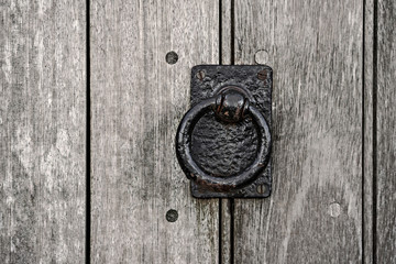 Old and heavy cast iron door knocker on a wooden door.