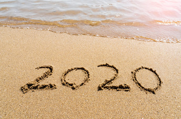 2020 year message handwritten in sand on beautiful beach background. New Years concept.