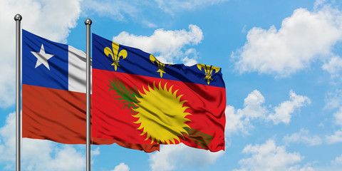 Chile and Guadeloupe flag waving in the wind against white cloudy blue sky together. Diplomacy...