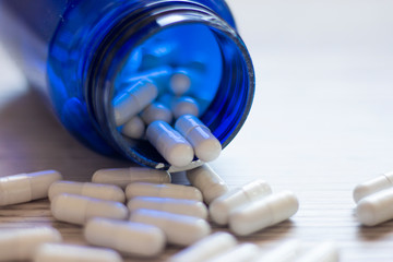 Blue medicine bottle with white pill capsules thrown on the table